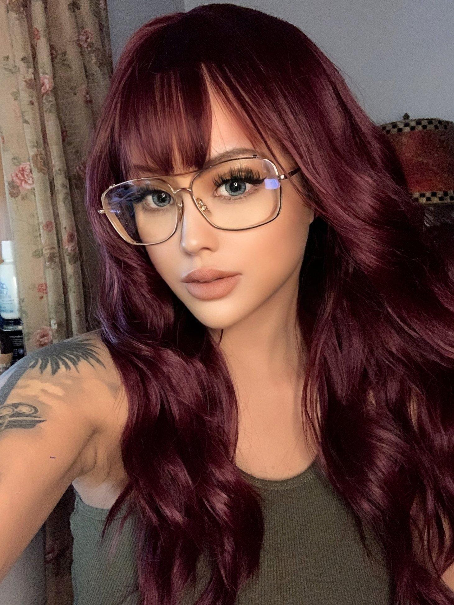 18 inch red wine wig by HAIRCUBE styled with loose waves and bangs on a model wearing glasses