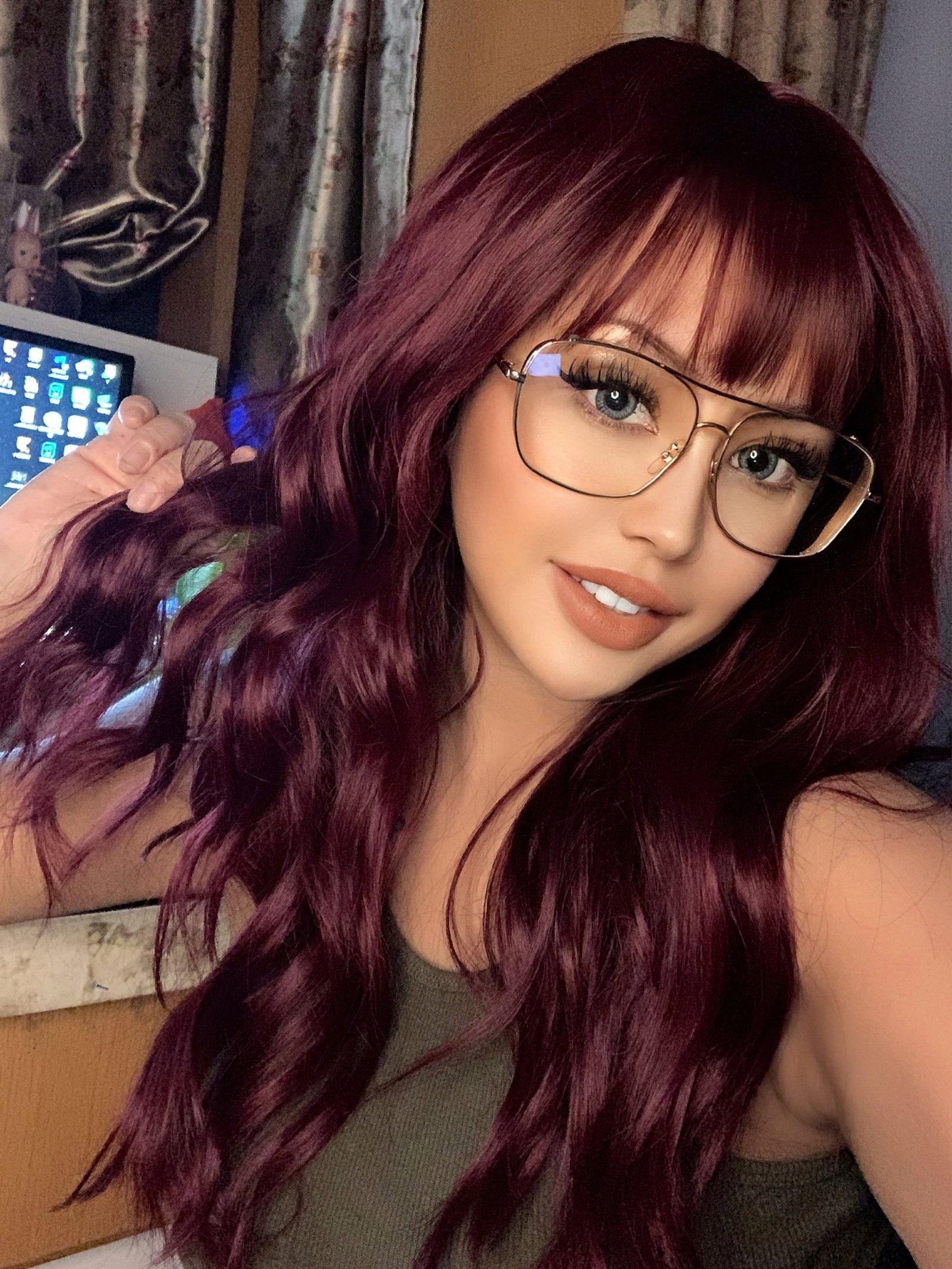 18 inch red wine wig by HAIRCUBE styled with soft waves and bangs on woman wearing glasses