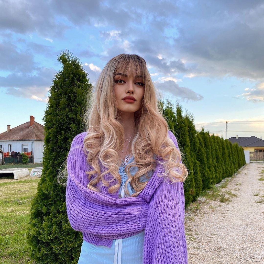 Blonde synthetic wig with bangs styled in loose curls worn by model outdoors