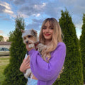 HAIRCUBE blonde synthetic wig with bangs styled in loose waves worn by woman holding small dog outdoors