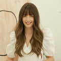 HAIRCUBE dark brown long curly synthetic wig worn by woman with bangs and white puff sleeve top