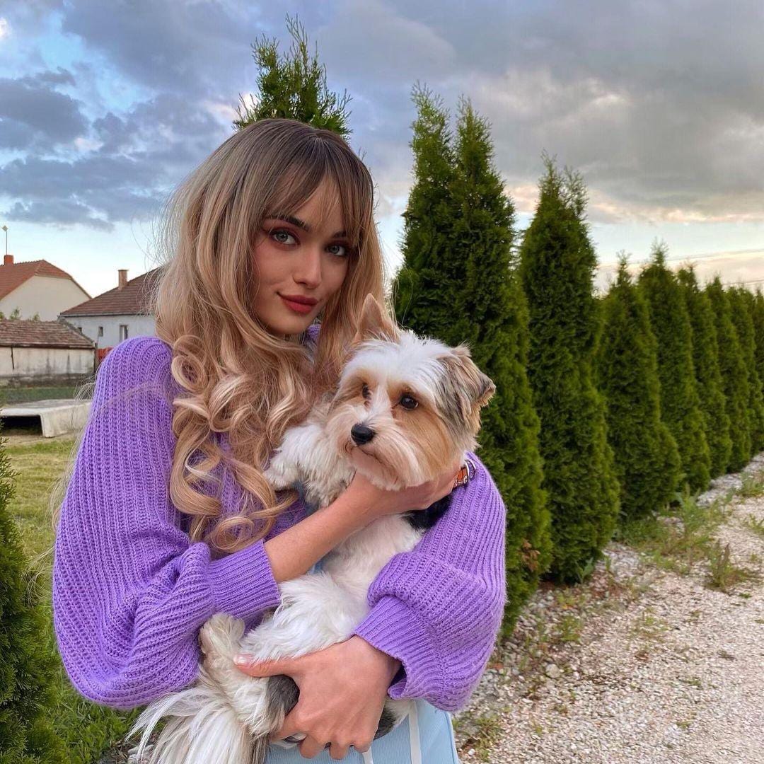 HAIRCUBE blonde synthetic wig with bangs worn by woman holding a small white and brown dog outdoors