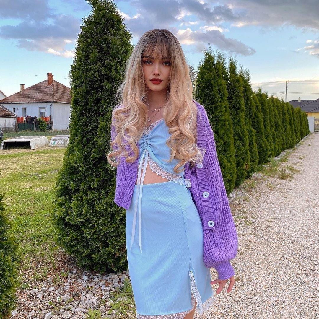 HAIRCUBE blonde synthetic wig with bangs styled in long loose curls on a woman outdoors