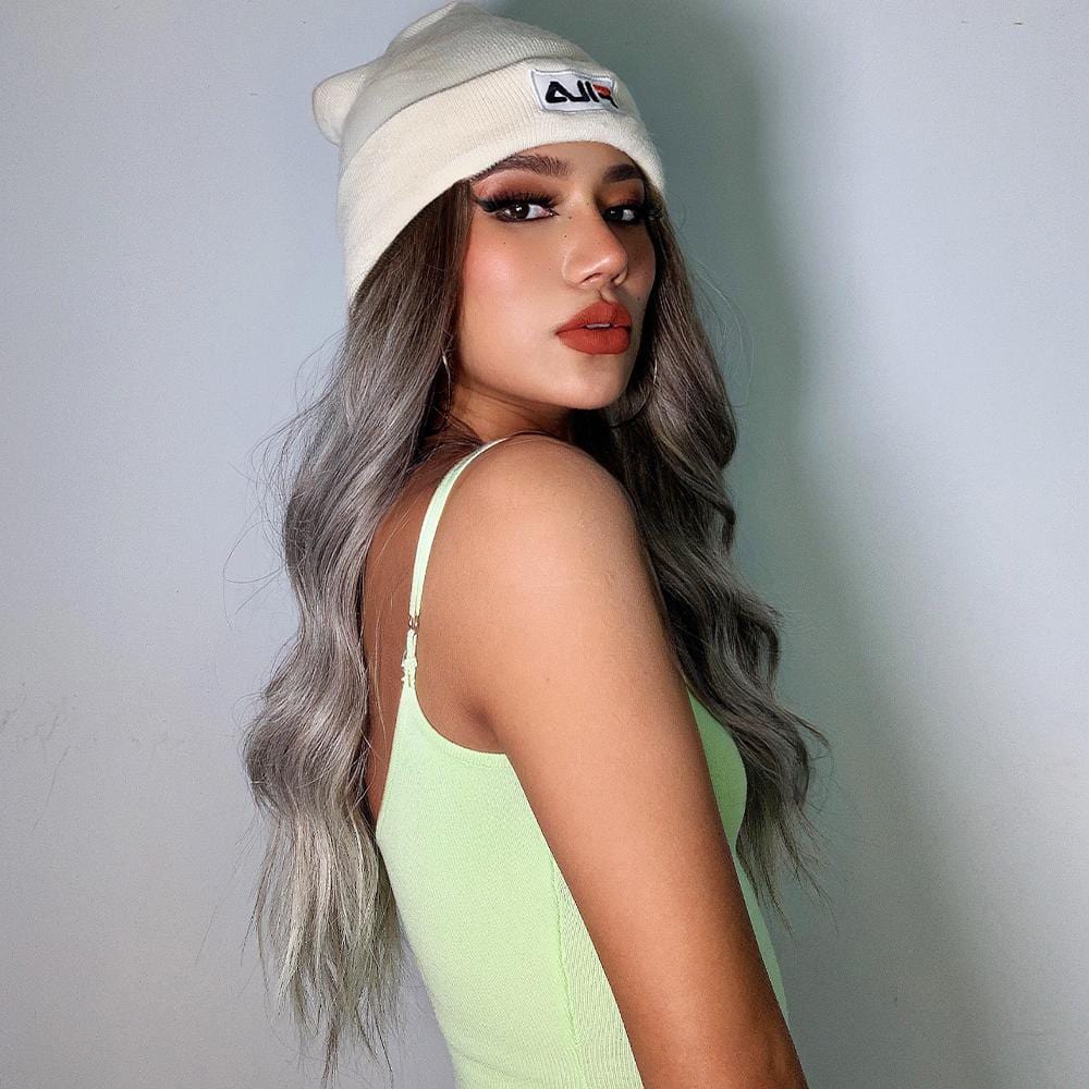HAIRCUBE smokey grey synthetic wig with long wavy hair worn by woman wearing a beige beanie and green tank top