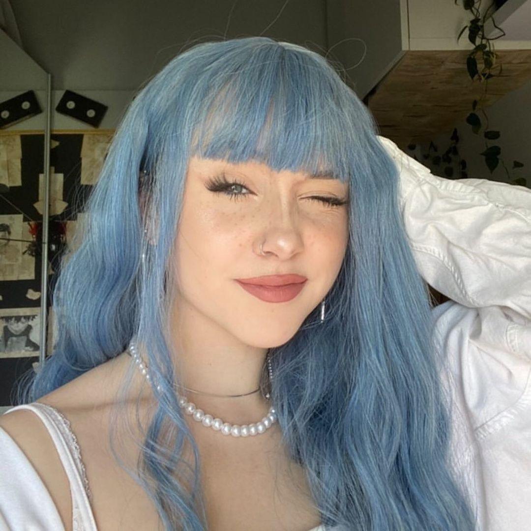 HAIRCUBE mermaid blue synthetic wig styled with bangs on woman wearing white top and pearl necklace