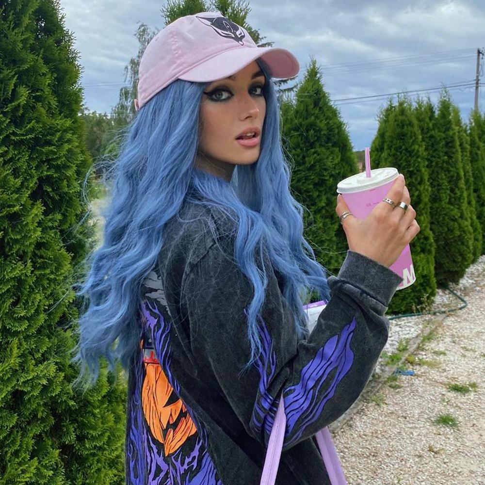 HAIRCUBE mermaid blue synthetic wig styled with long wavy hair worn with a pink cap outdoors